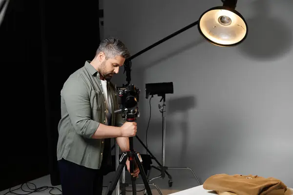 A skilled man prepares his camera on a tripod, focused on a work project under studio lights. — Stock Photo