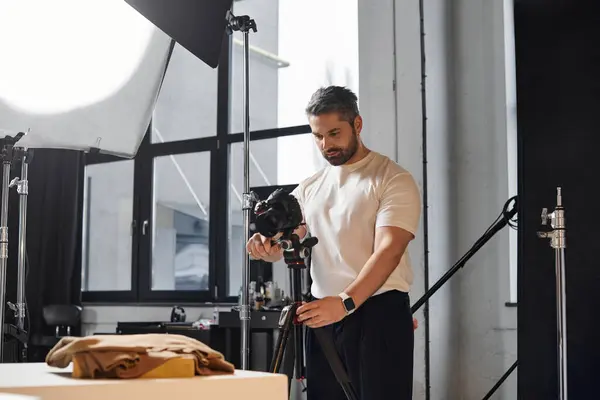 Avec une intention concentrée, un homme prépare son équipement de caméra dans un studio lumineux. — Photo de stock