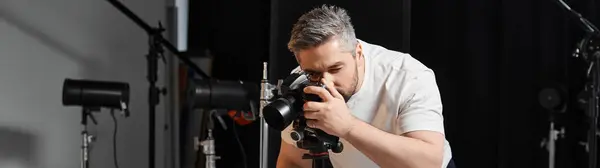 A dedicated man concentrates intently while adjusting a camera in a vibrant studio. — Stock Photo