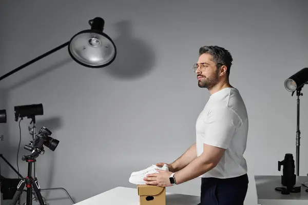 Ein Mann konzentriert sich darauf, einen Schuh zu präsentieren, während er von professioneller Beleuchtungstechnik umgeben ist. — Stockfoto