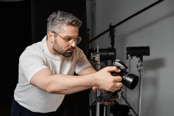 Individuo enfocado ajusta el equipo de la cámara mientras se prepara para una sesión de fotos creativa en interiores. - foto de stock