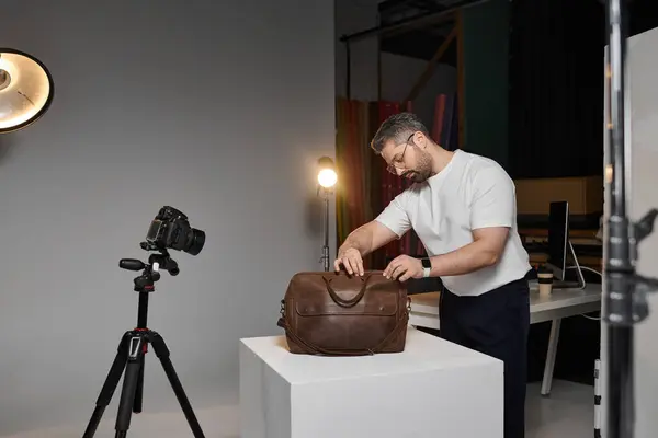 A man arranges a stylish bag on a pedestal while preparing for a creative project in a studio. — Stock Photo