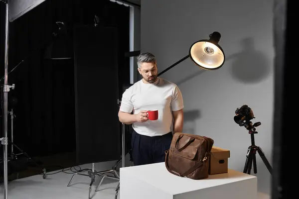 A man stands in a well lit studio holding a red cup of coffee, ready for his next project. — Stock Photo