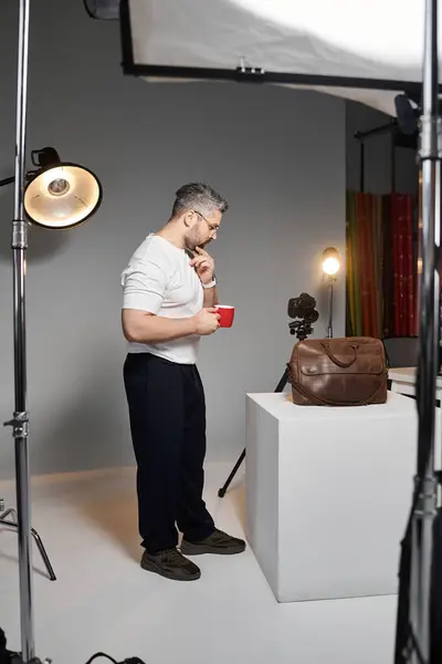 A man stands thoughtfully while holding a red cup, ready to work on a photography project. — Stock Photo
