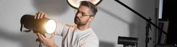 Man focuses intently on adjusting the lighting equipment in a professional photography studio. — Stock Photo