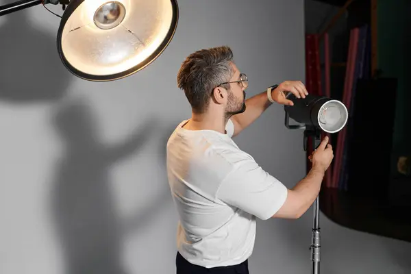 A man is focusing on adjusting the lighting equipment in a studio, preparing for a creative shoot. — Stock Photo