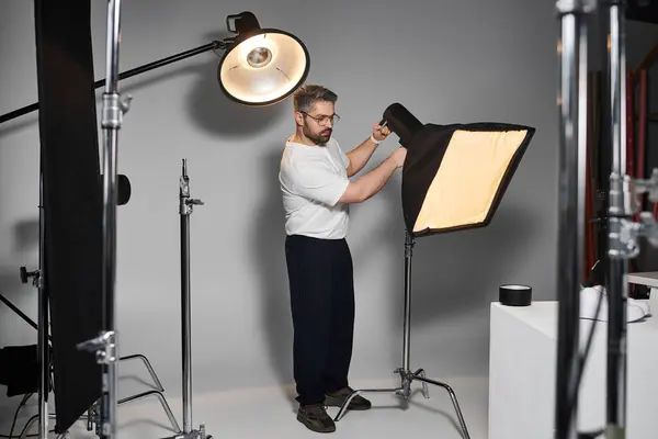 A dedicated man fine tunes lighting setup in a sleek studio as he prepares for an upcoming shoot. — Stock Photo
