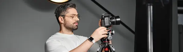 A skilled photographer focuses intently on adjusting his camera equipment in a well lit studio. — Stock Photo