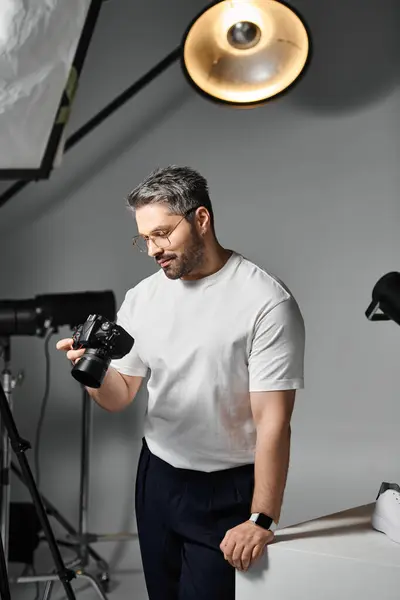A focused professional examines his camera in a well lit studio, ready to capture stunning visuals. — Stock Photo