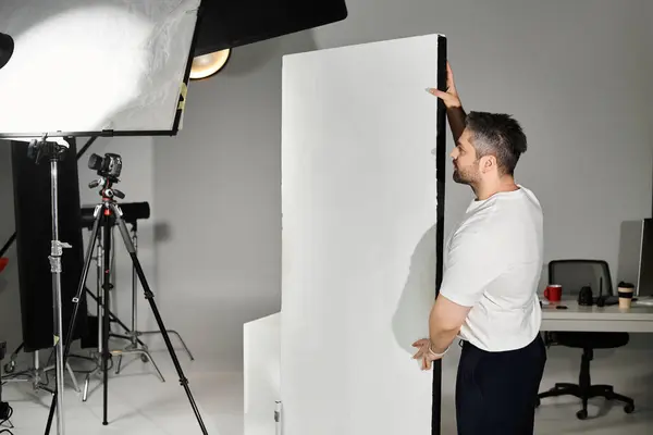 A man is skillfully adjusting a large white panel in a well lit studio, preparing for a project. — Stock Photo