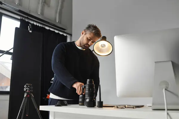 Un hombre dedicado ajusta su equipo de cámara mientras se enfoca en un ambiente de trabajo contemporáneo. - foto de stock