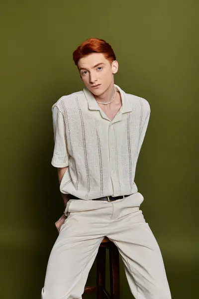 Un beau jeune homme aux cheveux roux s'assoit sur un tabouret, profondément réfléchi sur un fond vert. — Stock Photo