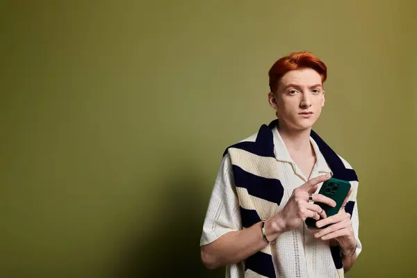 Captivating young man with striking red hair showcases emotion while holding his phone. — Stock Photo