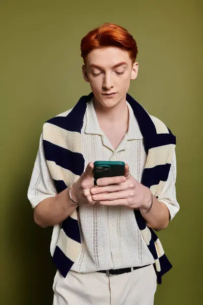 A beautiful young man dressed stylishly looks down at his phone, immersed in thought and feeling. — Stock Photo