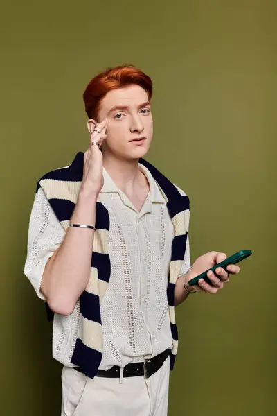 A confident young man showcases his emotions with a phone against a green backdrop. — Stock Photo