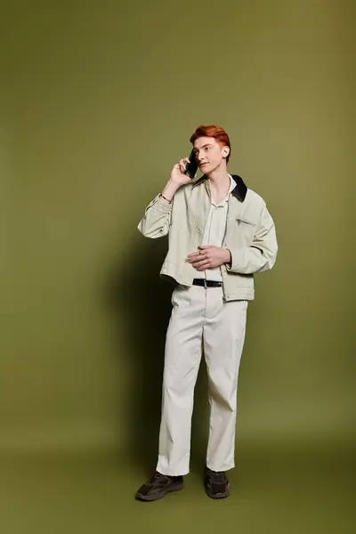 A young and handsome man stands thoughtfully on a green background while talking on his phone. — Stock Photo