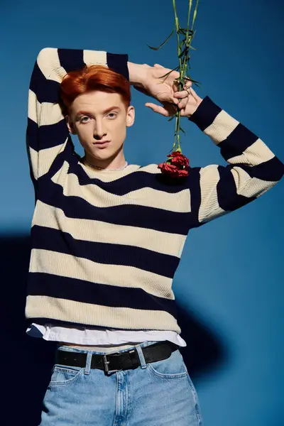 A young, handsome man in striped attire conveys emotion while showcasing a rose in his hands. — Stock Photo