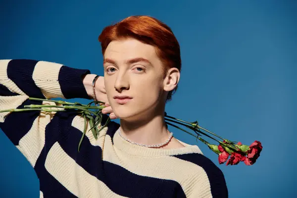 A handsome young man gracefully holds red flowers against a calming blue background. — Stock Photo