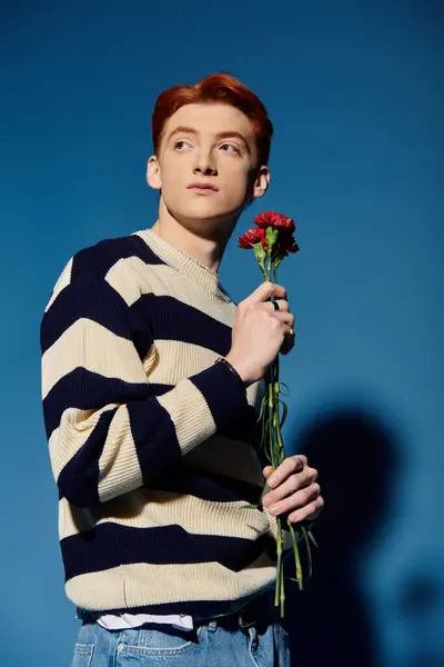 A handsome young man holds a flower, gazing thoughtfully into the distance. — Stock Photo