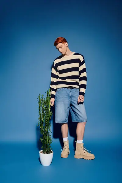 A young and handsome man expresses deep emotions while standing next to a plant indoors. — Stock Photo