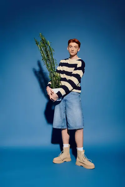 Emotional young man stands confidently in blue tones, cradling a lush green plant in his arms. — Stock Photo