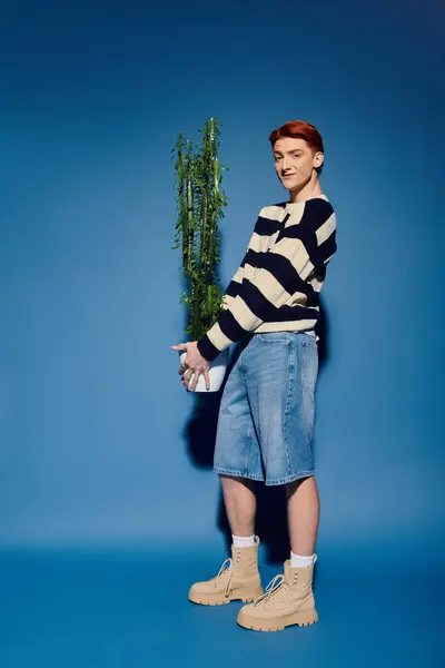 A young man smiles gently, cradling a vibrant green plant, revealing his emotional depth. — Stock Photo