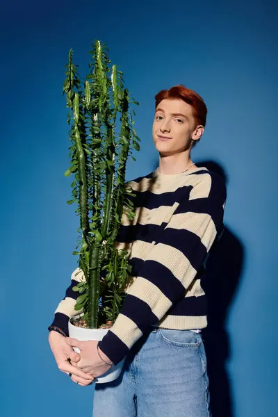 A young man with red hair expresses emotions while holding a large cactus in bright lighting. — Stock Photo