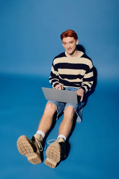 Handsome young man engages with his laptop, showcasing emotion and focus in a vibrant blue setting. — Stock Photo