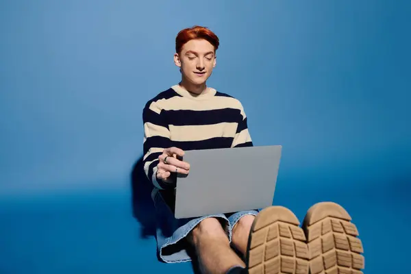 Un jeune homme aux cheveux roux vif s'engage avec son ordinateur portable, perdu dans la pensée et l'émotion. — Photo de stock