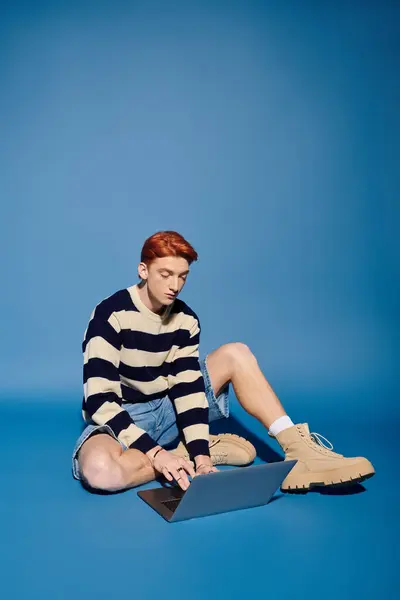 Emotional young man engages with his laptop, demonstrating concentration in a blue setting. — Stock Photo