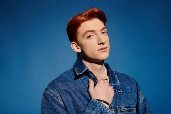 A young man with red hair shows deep emotions in a denim jacket against a blue backdrop. — Stock Photo