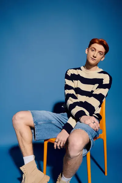 A young and handsome man with striking red hair sits on a chair, showcasing emotional depth. — Stock Photo