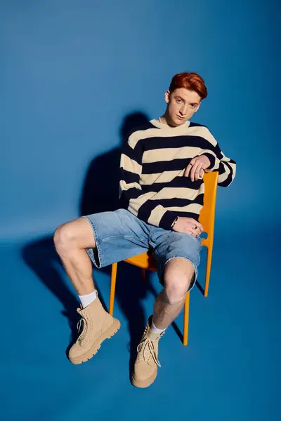 A young man with striking features sits in a chair, evoking emotion against a blue backdrop. — Stock Photo