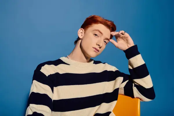A handsome young man with red hair expresses deep emotions while sitting against a blue background. — Stock Photo