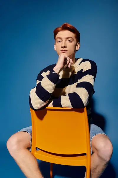 A young, handsome man with striking hair sits confidently, showing deep emotions in a modern space. — Stock Photo