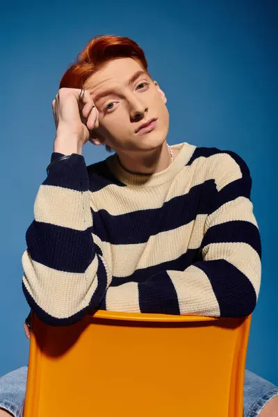 Young handsome man sits thoughtfully on a bright chair against a blue backdrop, exuding emotion. — Stock Photo