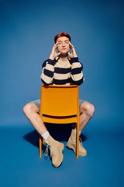 A handsome young man sits thoughtfully on a chair, showcasing emotions in a vibrant setting. — Stock Photo