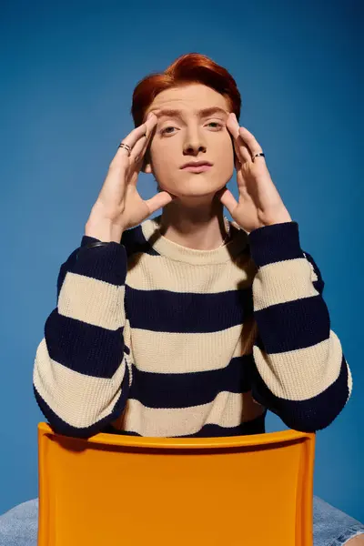 Un jeune et beau homme s'assoit délicatement, les mains sur le visage, entouré d'un fond bleu vif. — Photo de stock