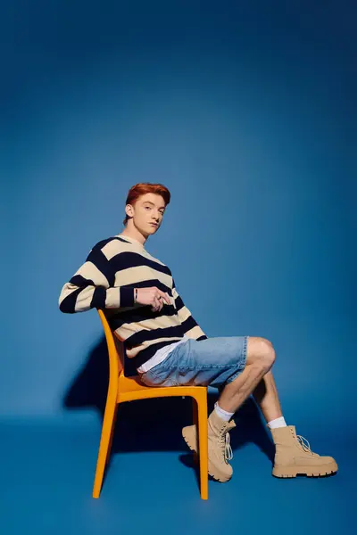 A handsome young man expresses deep emotion while sitting sideways in an orange chair. — Stock Photo