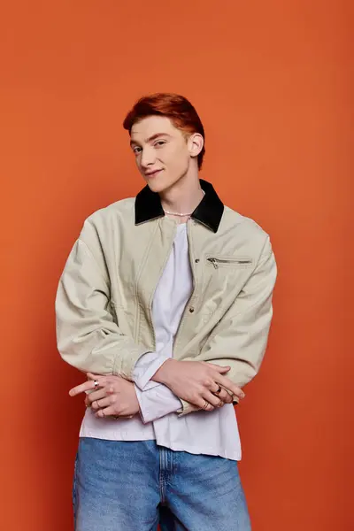 A young, handsome man with crossed arms exudes confidence in a bold orange setting. — Stock Photo