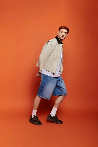 A young man showcases his style with a relaxed pose, expressing emotion and fashion against orange. — Stock Photo