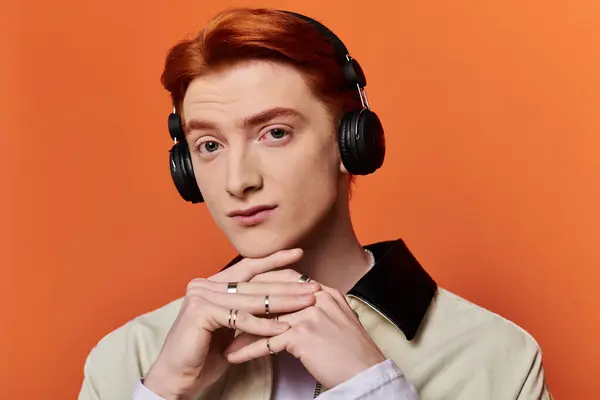 A young and handsome man contemplates while wearing headphones, framed by a bright orange wall. — Stock Photo