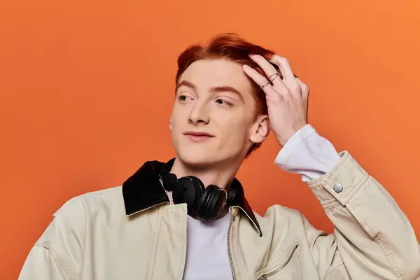 A young man adjusts his hair, lost in thought and deep emotions while wearing headphones. — Stock Photo