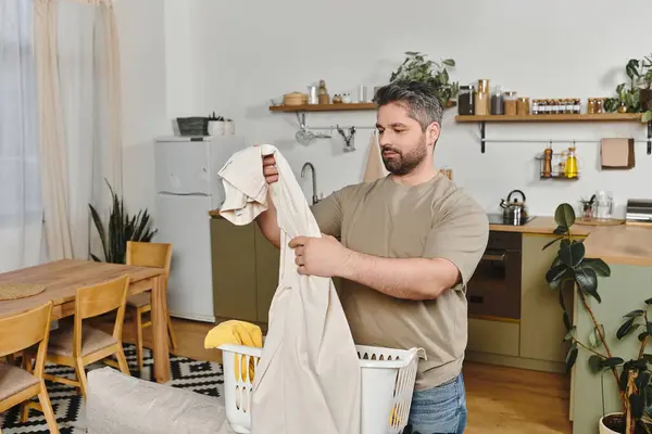 Ein Mann faltet sorgfältig saubere Kleidung in einer einladenden Küche, die Komfort und Leichtigkeit ausstrahlt — Stockfoto