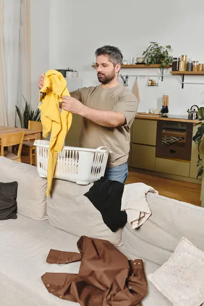 Ein Mann organisiert bunte Wäsche sorgfältig in seinem einladenden und gemütlichen Heim-Ambiente. — Stockfoto
