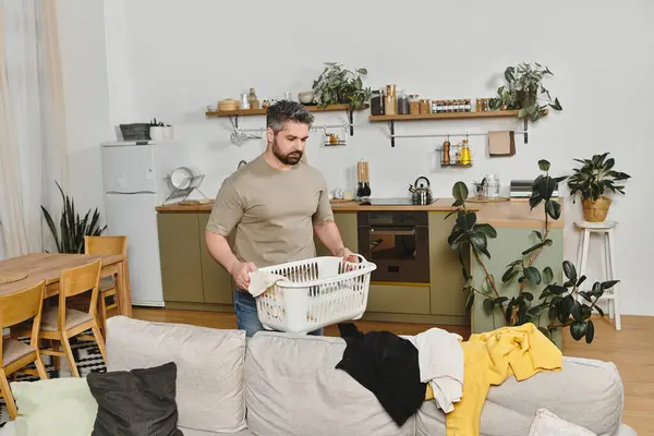 Ein Mann trägt einen Wäschekorb beim Aufräumen seines modernen und einladenden Wohnraums. — Stockfoto