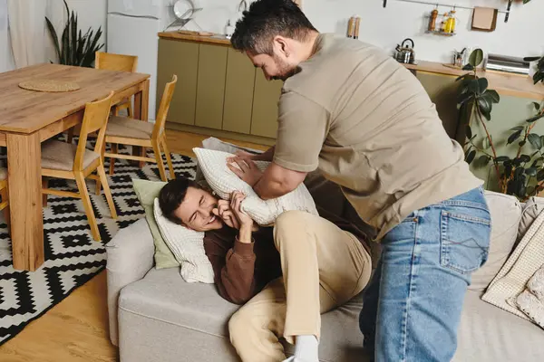 Two brothers engage in a lighthearted pillow fight on a comfortable couch, creating joy at home. — Stock Photo