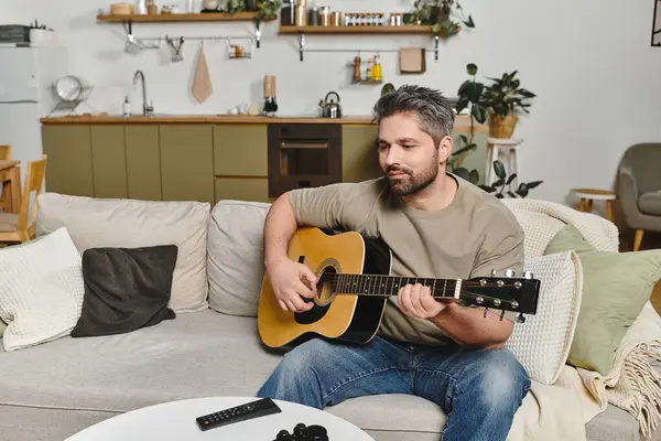 A man enjoys strumming his guitar on the sofa while surrounded by a warm and inviting interior. — Stock Photo