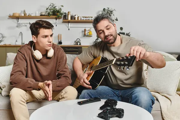 A man tunes his guitar while a young boy attentively listens in a warm living space. — Stock Photo