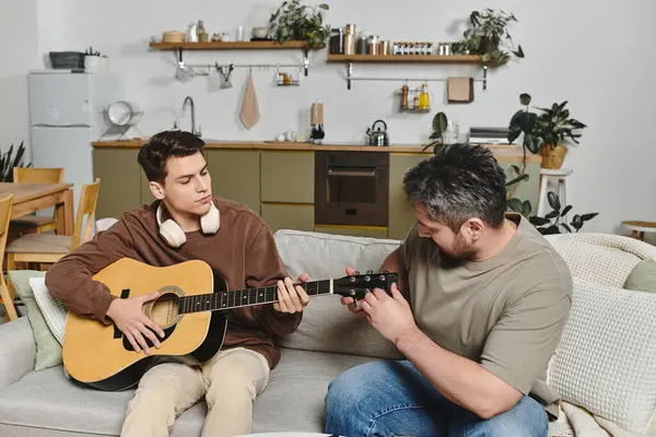 A young man is learning guitar basics from a caring adult at home, surrounded by comfort. — Stock Photo